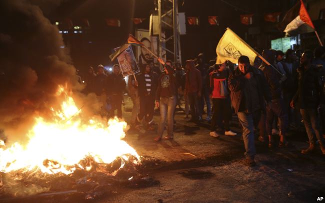 Người biểu tình Palestinian đốt lốp xe trong khi vẫy cờ Palestine và giơ hình của cố Tổng thống Palestine Yasser Arafat trong một cuộc biểu tình tại quảng trường chính ở Thành phố Gaza, ngày 6 tháng 12, 2017.